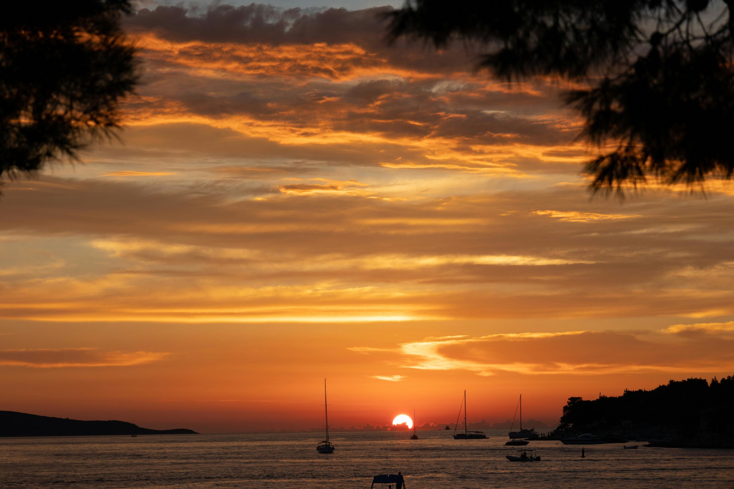 Scenic sunset view over Hvar, Croatia's coastline, with sailboats and vibrant clouds.